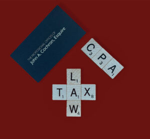 Expect Massive Delays in Processing Your Tax return This Year. An image of the John A. Cochran, Esq. re business card with scrabble pieces written out CPA and Tax Law.