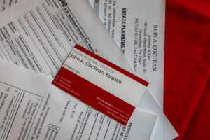 Expect Massive Delays in Processing Your Tax Return This Year. An image of the red and white John A. Cochran, Esquire business card and some tax forms.